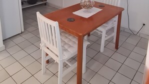 Cocina compacta con refrigerador, microondas y cafetera. Un comedor con sillas se ubica frente a un televisor de pantalla plana montado en la pared.