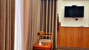 A hotel room with a TV mounted on the wall, a wooden chair, a small table with a glass, and a red bench. - Hien Lam Hotel (Ho Chi Minh City)