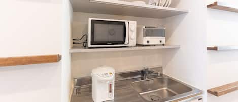 A compact kitchen with a microwave, toaster, and coffee maker on the countertop, and a sink with a faucet.