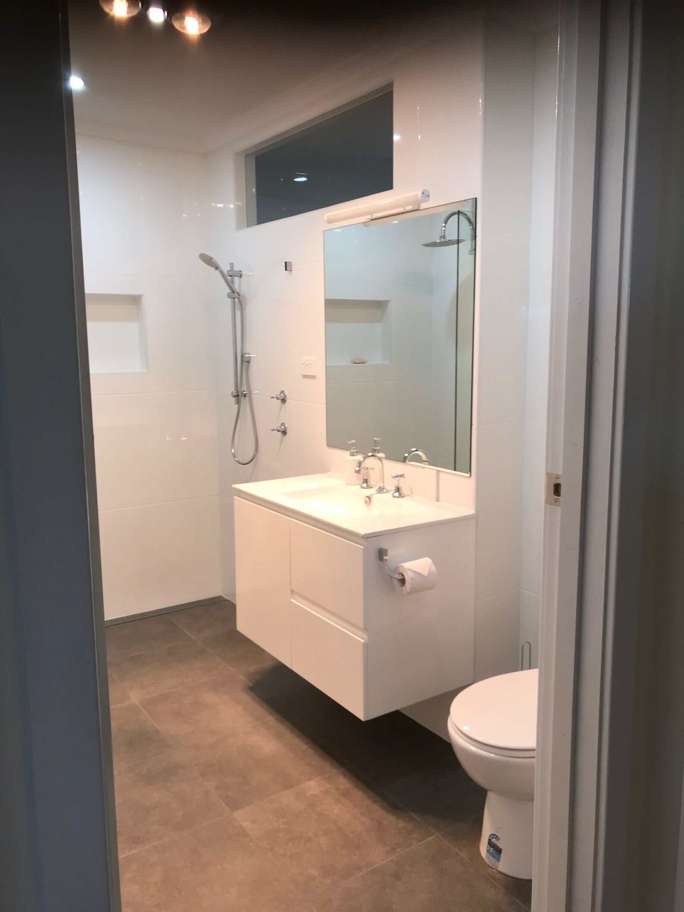 A modern bathroom with a walk-in shower, a large mirror, and a toilet.