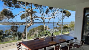 A dining table with chairs, a bottle, and wine glasses on a balcony with a view of the sea. - Wow! Kangaroo Island – Wildlife, Sunrises, Stunning Views, Spacious -Sleeps 13 (American River)