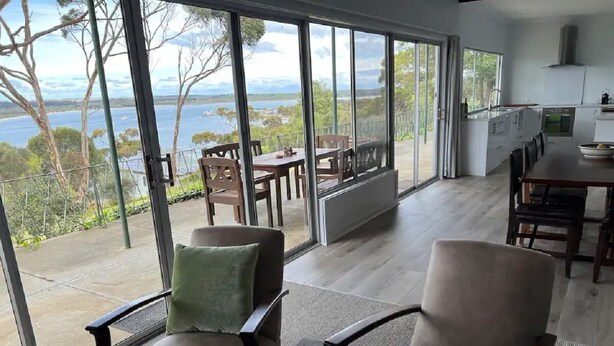 A spacious room with large windows offering a view of the outdoors. There are two armchairs and a dining table with chairs. - Wow! Kangaroo Island – Wildlife, Sunrises, Stunning Views, Spacious -Sleeps 13 (American River)