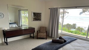 A bedroom with a bed, a dresser, a chair, a large mirror, and a window with a view of greenery. - Wow! Kangaroo Island – Wildlife, Sunrises, Stunning Views, Spacious -Sleeps 13 (American River)