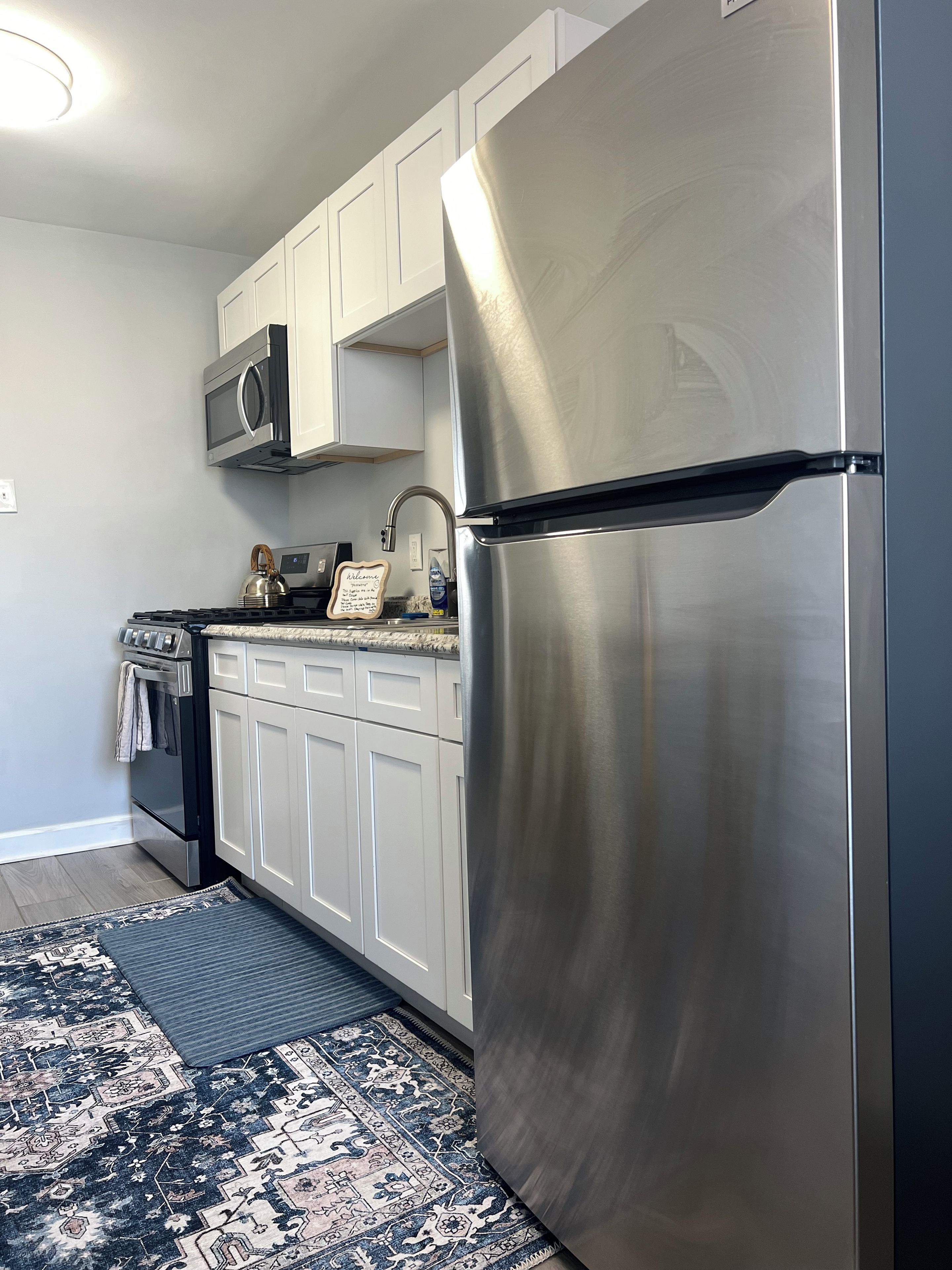 A kitchen with white cabinets, a stainless steel refrigerator, a microwave, and a stove.