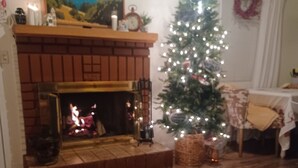 Un salon chaleureux avec une cheminée, un sapin de Noël et un tableau accroché au mur.