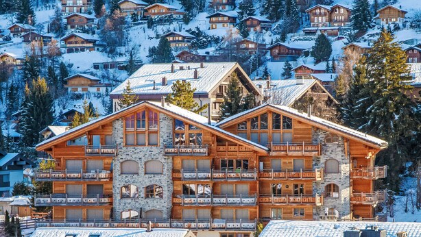 Ein mehrstöckiges Chalet mit Balkonen, einer Steinfassade und verschneiter Umgebung.