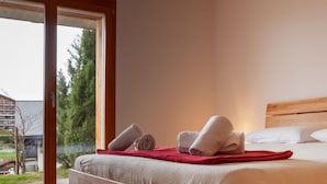 Ein Schlafzimmer mit einem hölzernen Bett, einer roten Decke und einem Fenster mit Blick auf Bäume und Gebäude.