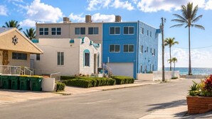 A coastal building with a blue and beige facade, a clear sky, and palm trees.