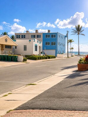 Un bâtiment situé sur la côte, avec une façade bleue et beige, un ciel dégagé et des palmiers.