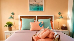 A neatly made bed with a basket of towels, two nightstands with lamps, a wall-mounted picture, and a potted plant.