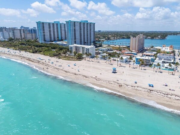 A beachfront hotel with a sandy beach, ocean view, and high-rise buildings in the background.