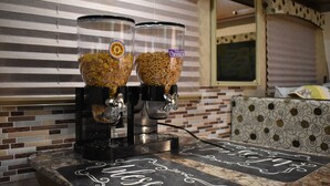 Un coin cuisine équipé de deux distributeurs de céréales, d’une machine à café et d’un tableau noir sur lequel est écrit le mot « Souhaits ».