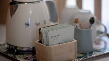 Una tetera blanca con el nombre de marca "SME" sobre una bandeja con un bloque de madera que sostiene una bolsita de té etiquetada como "Té Desayuno Inglés Orgánico".