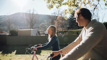 Una persona montando una bicicleta rosa en un patio trasero con una valla de madera y árboles al fondo.