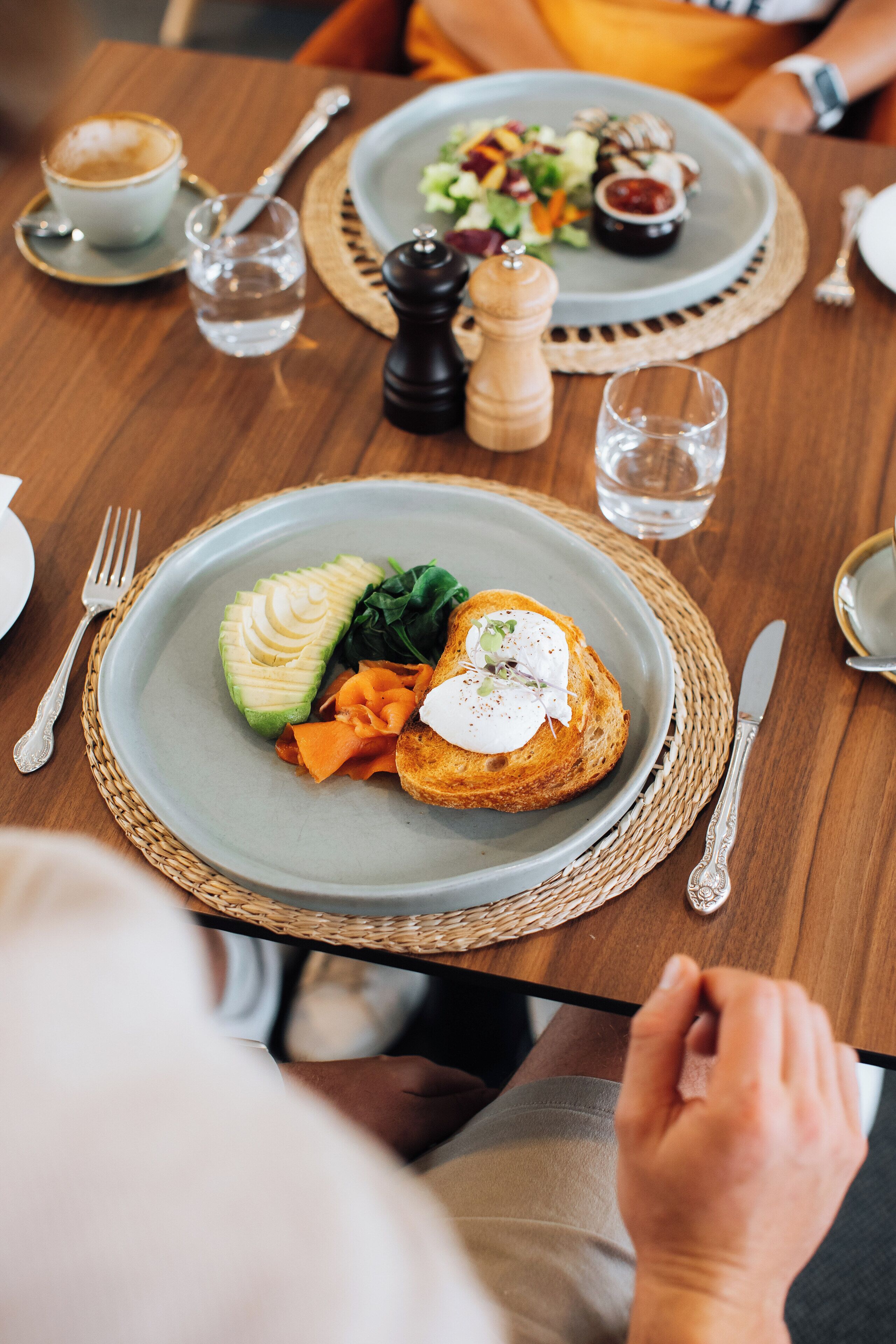 A dining table with plates of food, a cup of coffee, and a salt and pepper shaker.