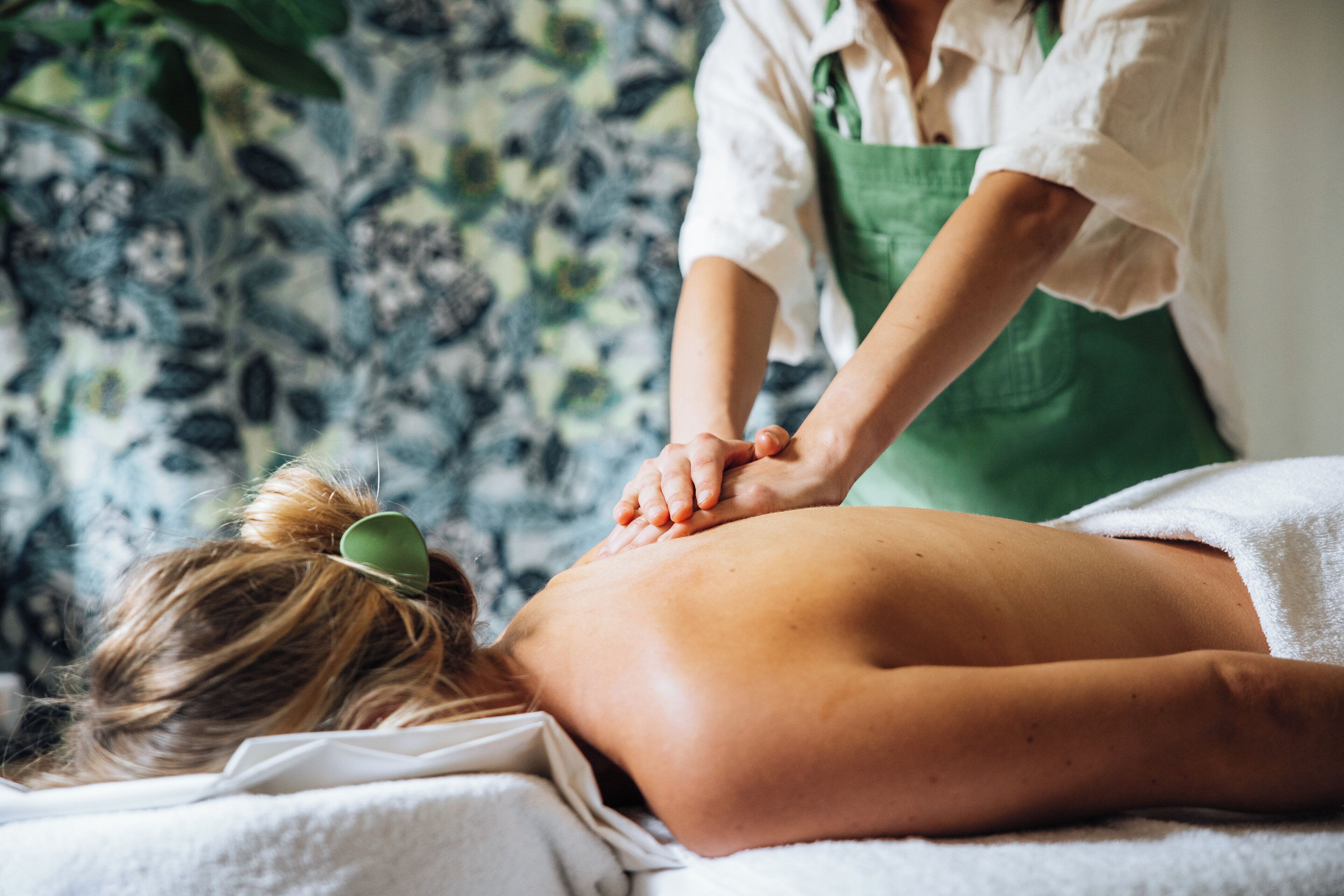 A person receiving a back massage in a room with a patterned wall.