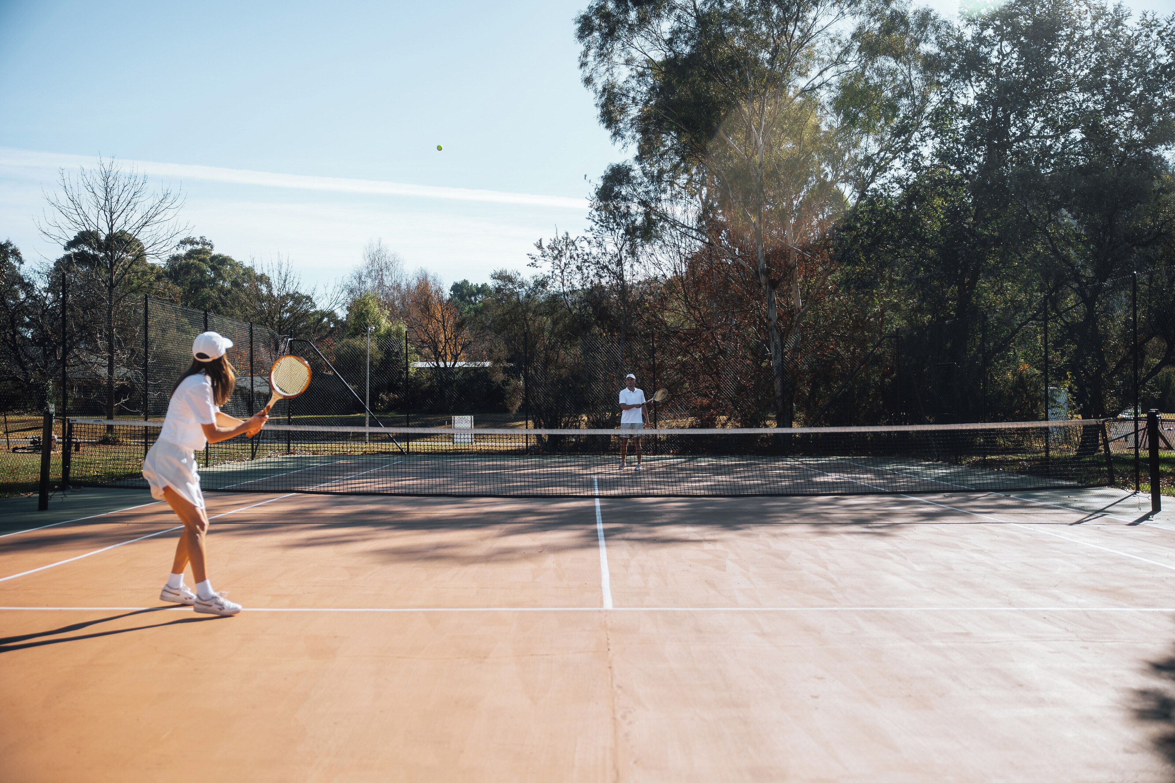 A tennis court with a net, trees, and a clear sky.