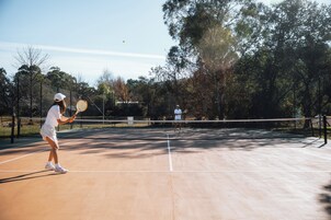 Una cancha de tenis con red, árboles y cielo despejado.