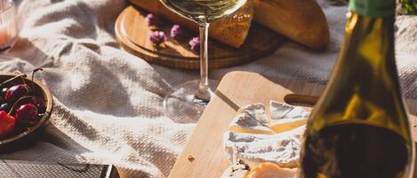 A picnic setup with a bottle of wine, a glass, cheese, bread, and a book on a blanket.