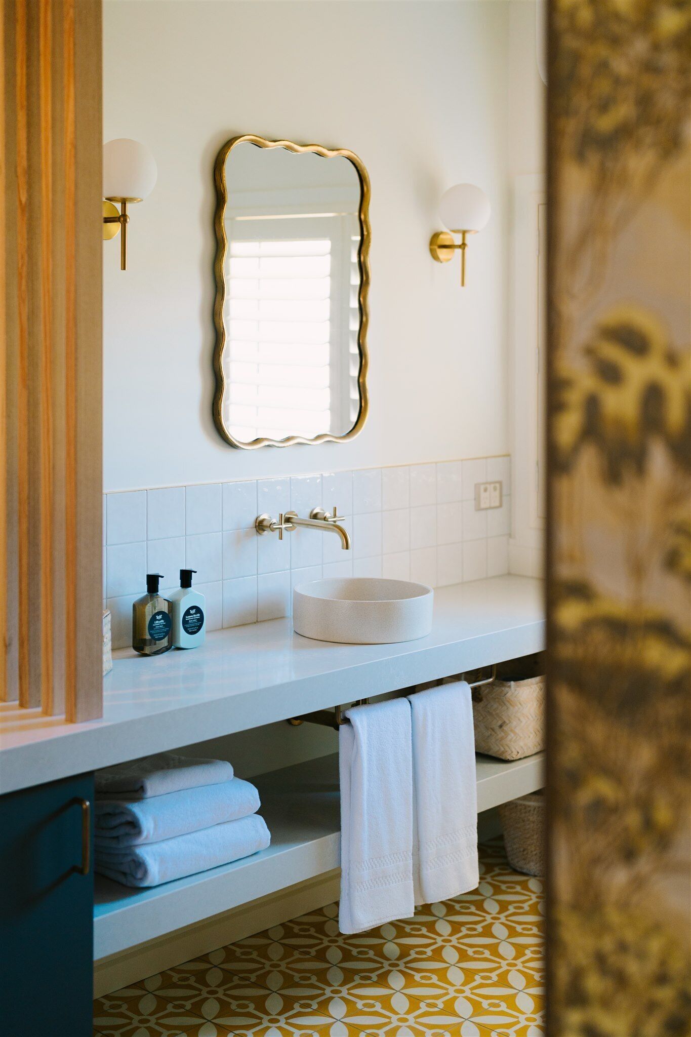 A bathroom with a white sink, gold fixtures, and a decorative mirror.