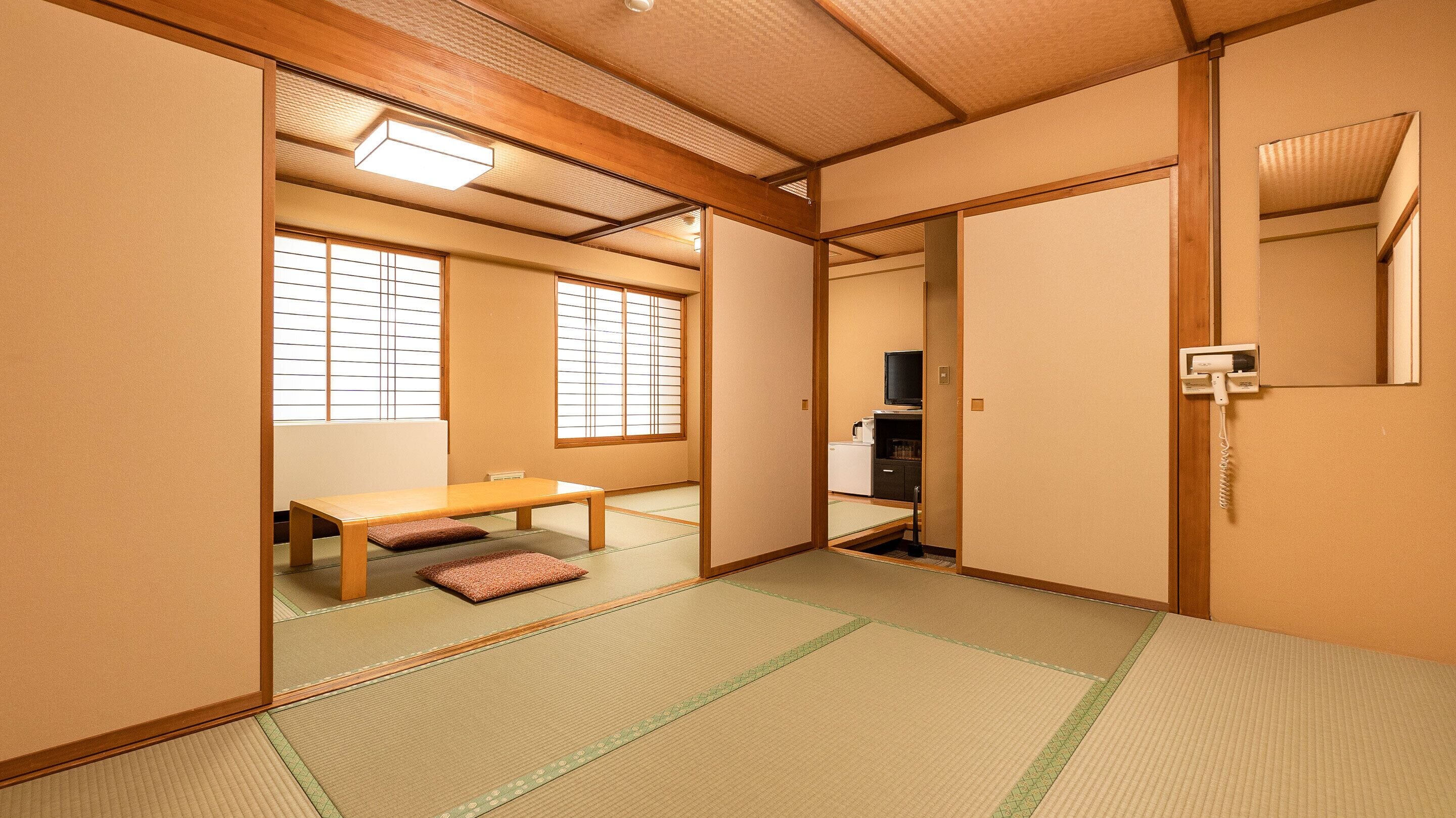 Une pièce de style japonais traditionnel, avec un sol recouvert de tatamis, une table basse avec des coussins, des portes coulissantes et un téléviseur.