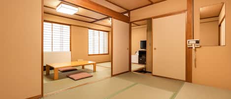 Une pièce de style japonais traditionnel, avec un sol recouvert de tatamis, une table basse avec des coussins, des portes coulissantes et un téléviseur.