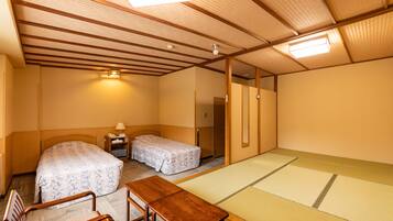 A traditional Japanese-style room with tatami flooring, two single beds, a wooden table, and a small desk with a lamp.