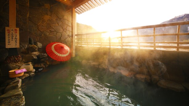 A traditional Japanese onsen with a stone wall, a wooden ceiling, and a view of a mountain through a window. - Ooedo Onsen Monogatari Kounkaku (Osaki)