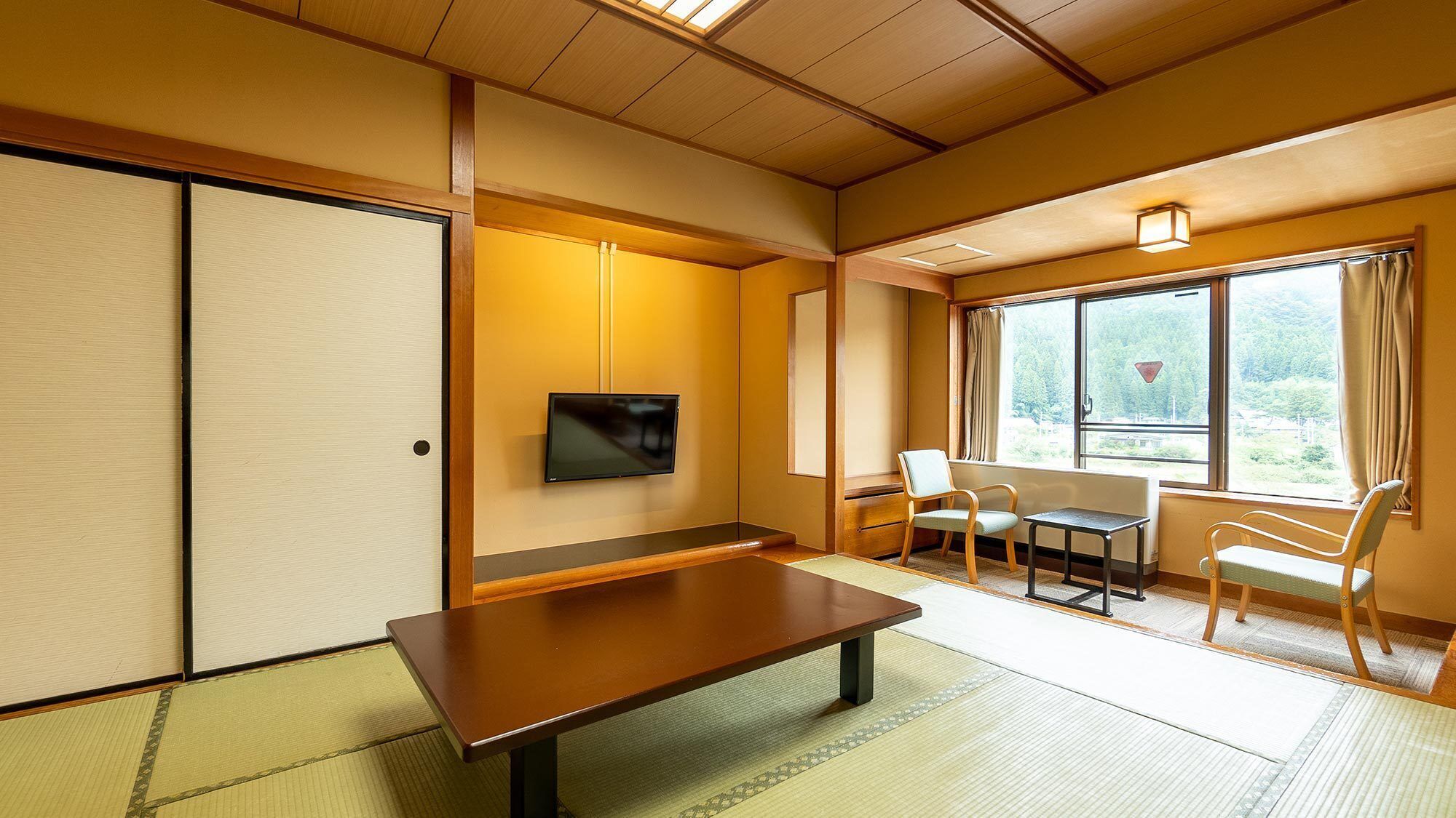 Une pièce de style japonais traditionnel, avec un sol recouvert de tatamis, une basse table en bois, un téléviseur et une fenêtre donnant sur un paysage verdoyant.