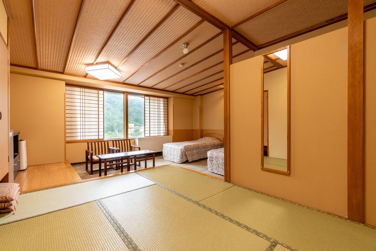Una habitación japonesa tradicional con suelo de tatami, una mesa de madera baja, una cama con colcha estampada y un espejo grande en la pared.