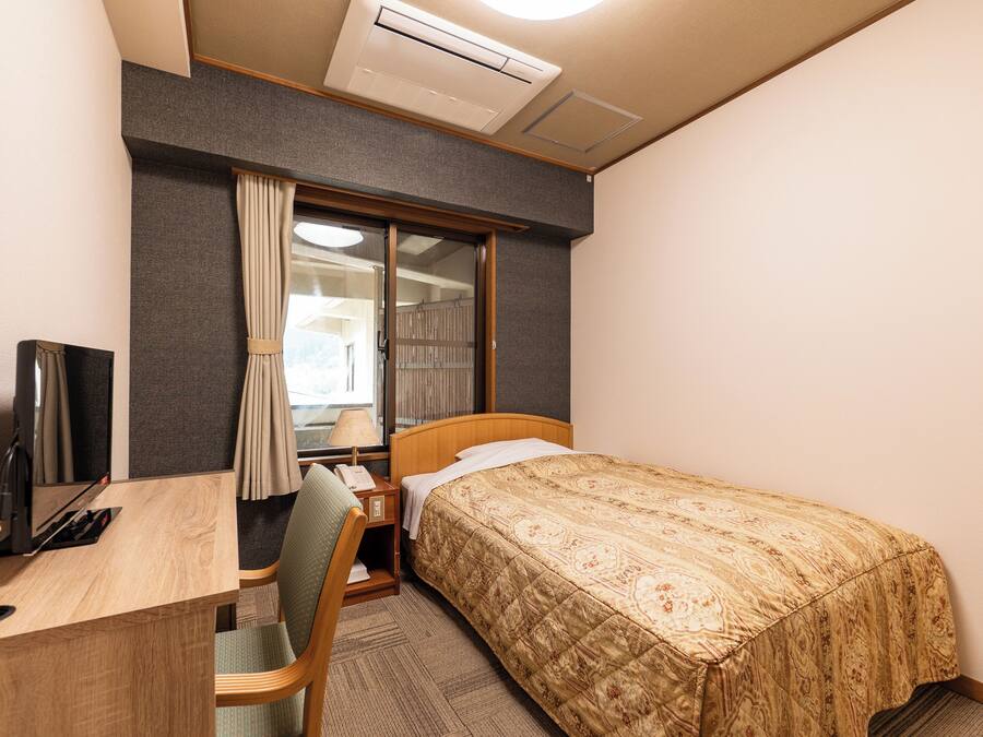 A hotel room with a bed, desk, chair, and a television.