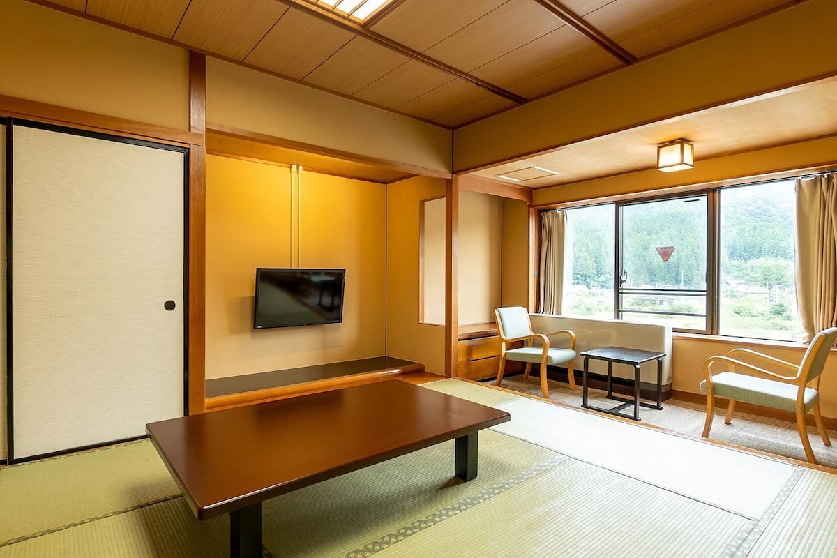 Una habitación tradicional japonesa con suelo de tatami, una mesita baja, un televisor y una ventana con vistas.