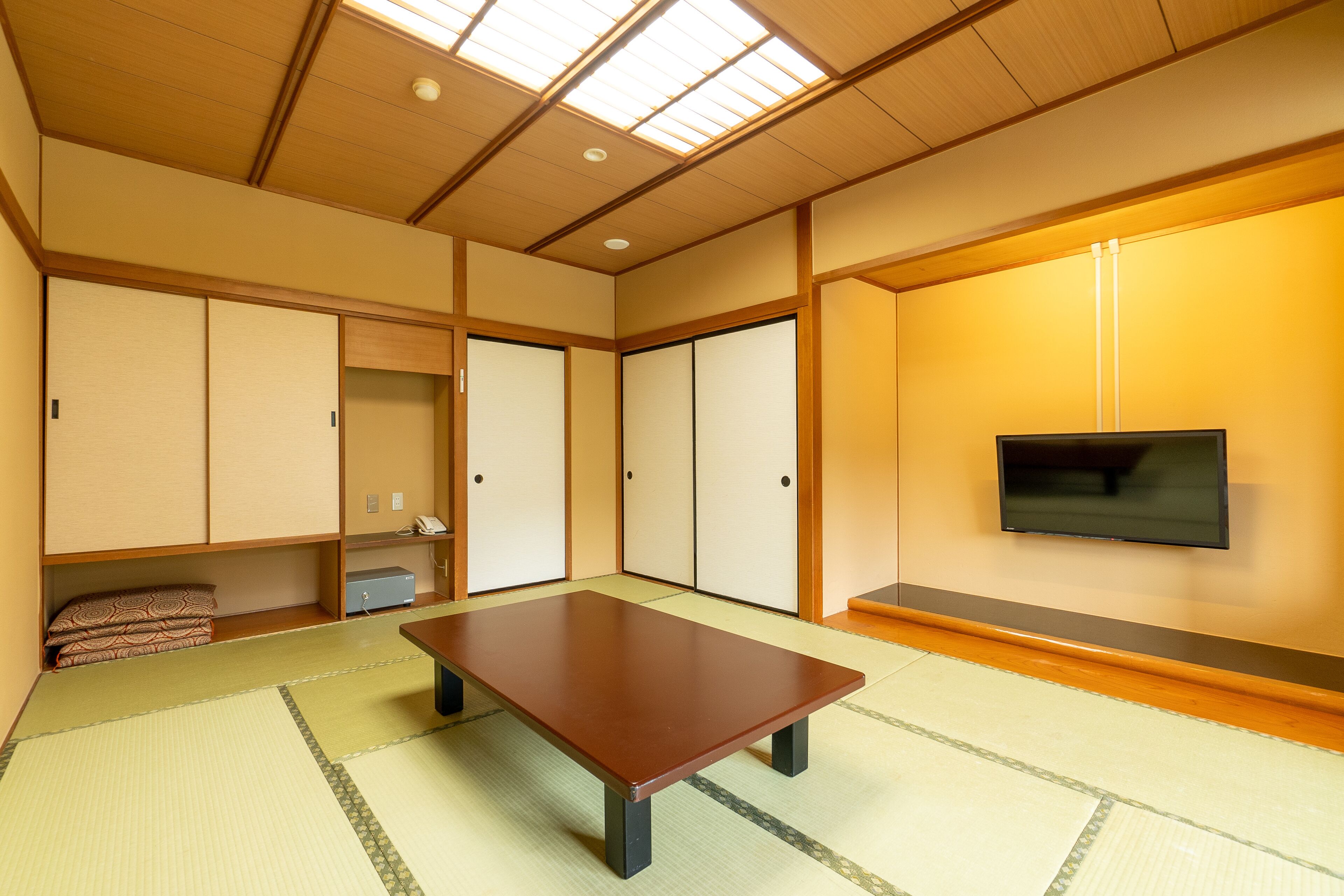 Een traditionele Japanse kamer met tatami vloeren, een lage tafel, schuifdeuren en een televisie aan de muur.