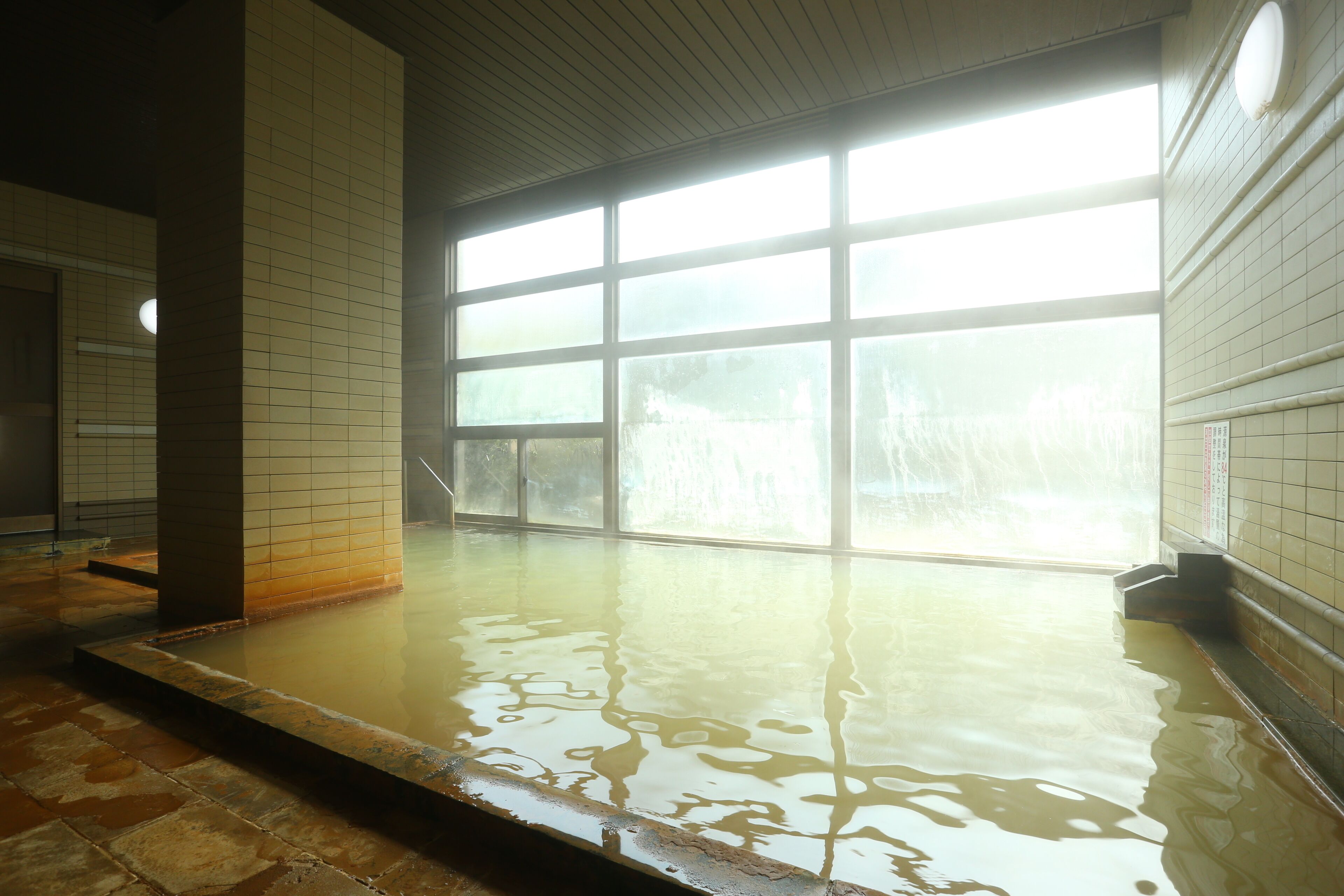 Una amplia piscina interior con ventanas de vidrio transparente, paredes y piso de azulejos.