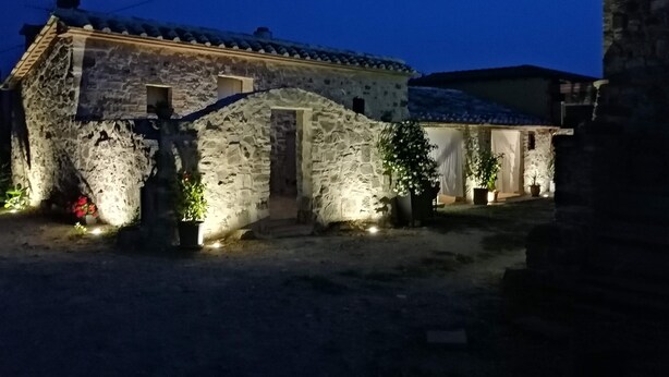 A stone house with a tiled roof, a small porch, and potted plants.