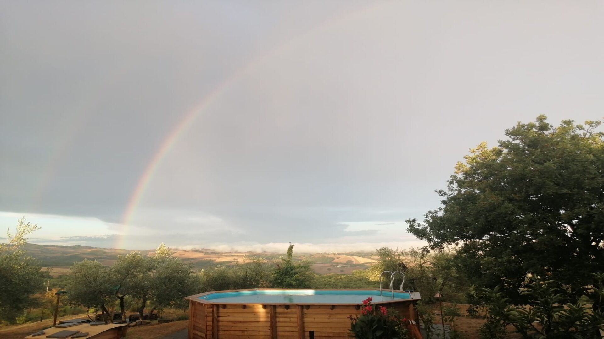 Una vasca idromassaggio in legno con vista sulla valle e un arcobaleno nel cielo.