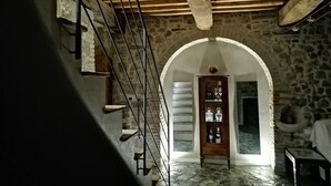 A stone-walled hallway with a wooden staircase and an arched doorway.