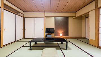 Una habitación japonesa tradicional con suelo de tatami, una mesa baja, un cojín y puertas correderas.