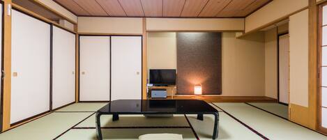 Um quarto japonês tradicional com tatames, uma mesa baixa, um travesseiro e portas deslizantes.