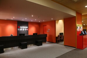 Ein Empfangsbereich mit einer schwarzen Theke, roten Wänden und einer kleinen Sitzecke mit Stuhl und Tisch.