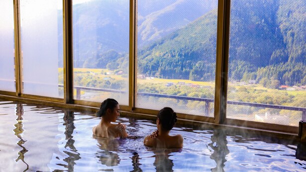 Two people in a hot tub with a mountain view through large windows. - Ooedo Onsen Monogatari Masuya (Osaki)