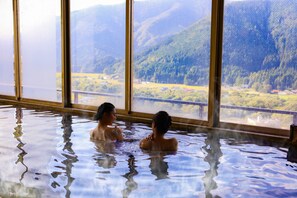 Dos personas en un jacuzzi con vistas a la montaña a través de grandes ventanales.
