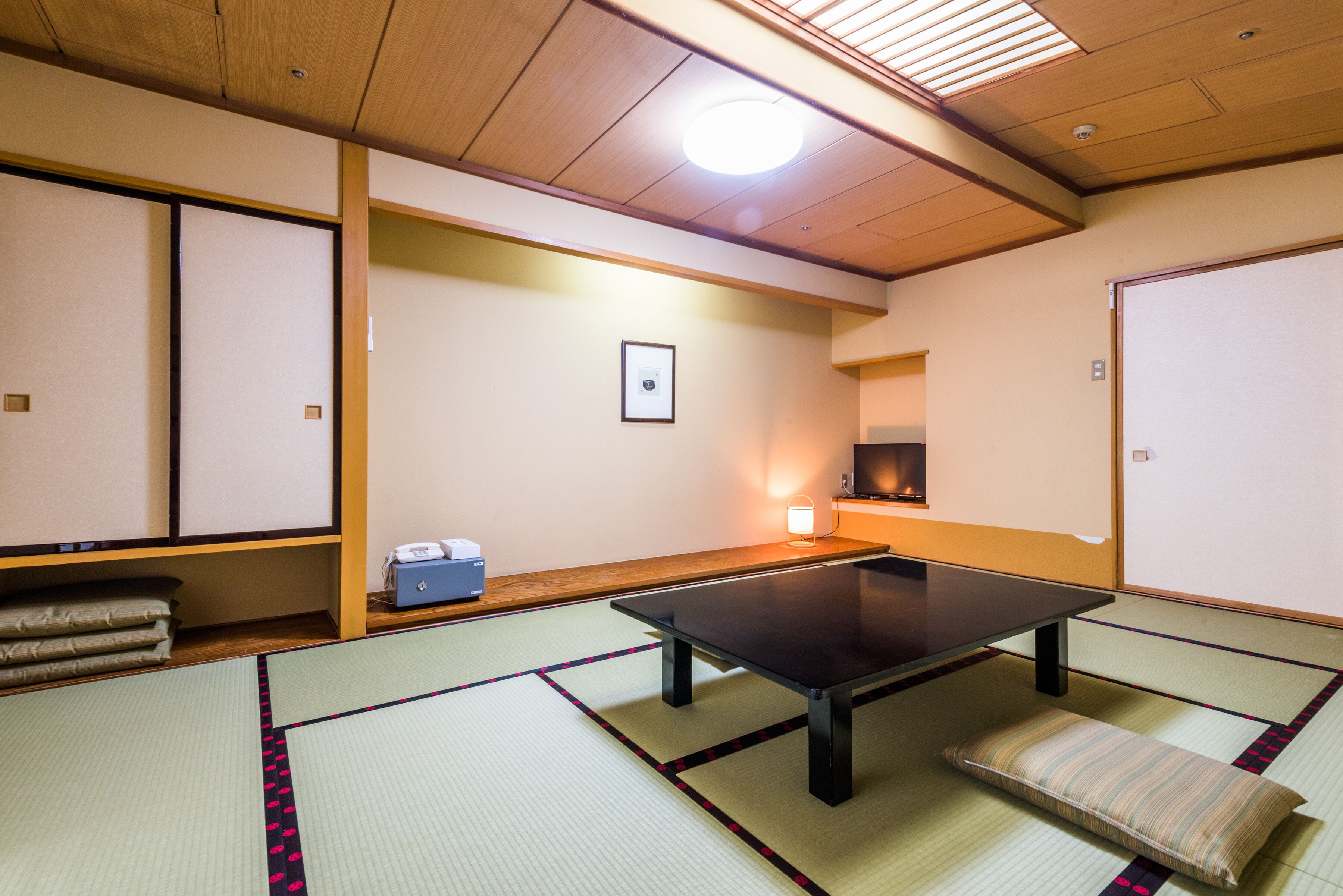 Een traditionele Japanse kamer met tatami vloerbedekking, een lage tafel, kussens en een schuifdeur.