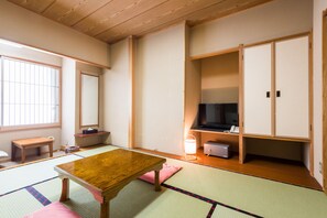 Ein traditioneller japanischer Raum mit Tatami-Bodenbelag, einem Holztisch, einem Fernseher und einem Kleiderschrank.