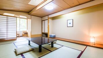 A tatami mat room with a low table, a pillow, a picture on the wall, and a window with a view of trees.