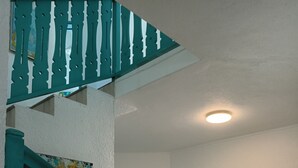 Un escalier avec des rampes de couleur turquoise menant à une pièce où se trouvent une horloge et une œuvre d’art murale aux couleurs vives.