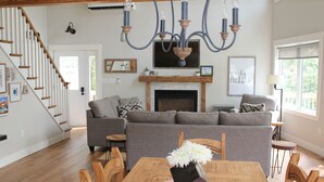 A spacious living room with a fireplace, a dining table with chairs, a grey sofa, and a staircase. - 4-bedroom house in Stanhope - walk to the beach! (York)