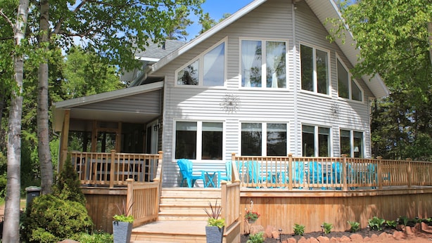 A two-story house with a deck, large windows, and a covered porch area. - 4-bedroom house in Stanhope - walk to the beach! (York)