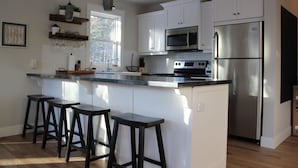 A kitchen with white cabinets, a stainless steel refrigerator, a microwave, and a large island with bar stools. - 4-bedroom house in Stanhope - walk to the beach! (York)