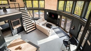 Un interior moderno con techo de madera, ventanas amplias, una escalera, una zona de estar y un televisor.